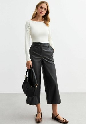 Top blanco de manga larga, pantalones anchos de imitación cuero negros con bolsillos frontales y bailarinas de estampado de leopardo. Bolso negro con un diseño curvado.