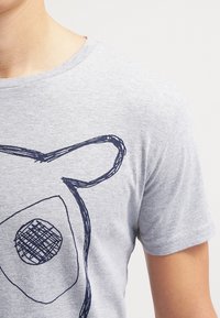 Camiseta gris de tela suave con un gran gráfico de cara de animal dibujado a mano en azul marino. Cuello redondo y mangas cortas.