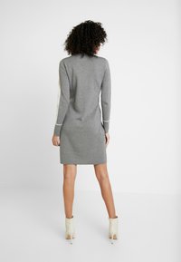 Abito a maglia grigio con forma aderente, maniche lunghe e dettagli in rete sui lati. Notevole per il suo design semplice e la texture morbida, arricchito da accenti crema.