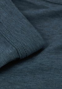 Tyrkysová, texturovaná tkanina s jemným, mírně melírovaným vzhledem. Hladké okraje s viditelným šitím. Vhodné pro každodenní nošení.