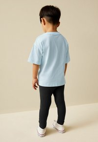 Svetlomodré bavlnené tričko s krátkymi rukávmi, v kombinácii s čiernymi rebrovanými legínami a bielymi teniskami, pohľad zozadu.