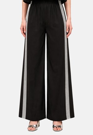 Schwarze, weit geschnittene Hose mit weißen vertikalen Streifen an den Seiten, elastischem Bund, getragen mit silbernen offenen High-Heel-Sandalen.