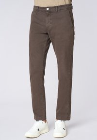 Pantaloni di cotone marroni con vestibilità dritta, tasche frontali e chiusura con bottone in vita, abbinati a sneakers bianche.