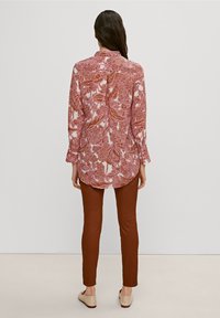 Langärmelig, roze met witte bloemenblouse met een ontspannen pasvorm en een afgeronde zoom. Gecombineerd met strakke bruine broeken en beige flats.