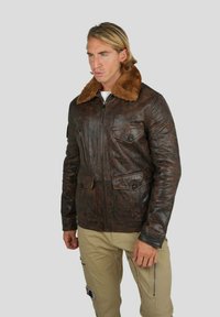 Veste en cuir marron avec un col en fourrure beige, présentant une fermeture éclair à l'avant, deux poches poitrine et deux poches plaquées inférieures. Texture lisse et design durable.