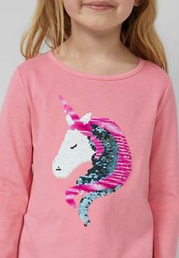 Dziecko w różowej koszulce z cekinowym wzorem jednorożca w kolorze białym, różowym i niebieskim na przedzie.