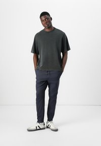 Dark gray oversized T-shirt with short sleeves, paired with navy tapered joggers and white sneakers featuring black stripes.