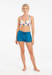 Farebný plavkový top s hlbokým výstrihom do V a nastaviteľnými ramienkami, spárovaný s jednotvárnymi tyrkysovými plavkovými šortkami s čipkovým lemovaním a šnúrkou na stiahnutie.