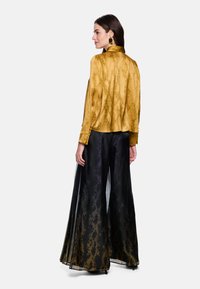 Yellow snake-patterned blouse with a high collar, paired with black, flared trousers that feature a subtle gradient and sheer overlay.