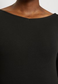 Svart, åtsittande topp gjord av ribbat tyg. Har en bred, öppen halsringning med lätt sömnadsdetalj. Slät yta, kroppsnära design.