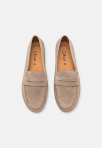Beige ruskind slip-on loafers med flad sål, der har et dekorativt syet bånd over fronten og en glat læderindersål.