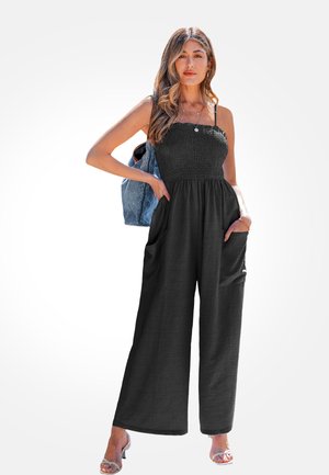 Combinaison noire sans bretelles avec un buste smocké, design à jambes larges, texture douce et poches latérales. Un sac à dos en denim gris sert d'accent.
