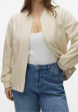 Veste bomber beige clair avec des poignets côtelés, fermeture éclair et une texture lisse, assortie à un jean en denim bleu taille haute.