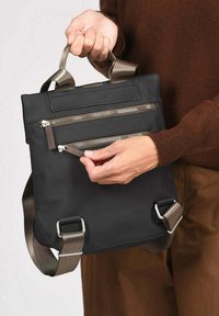 Bolso negro con múltiples bolsillos con cremallera, asas de acabado satinado y correa ajustable. Fabricado con un material duradero y un diseño elegante.