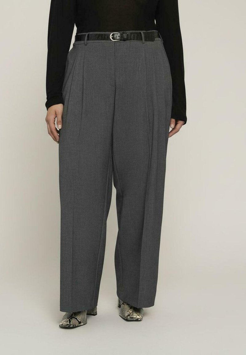 Szare plisowane spodnie z wysokim stanem i czarnym paskiem, o dopasowanym kroju. Noszone z wzorzystymi botkami dla dodatkowego efektu.