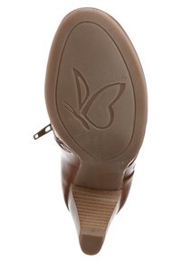 Chaussure à talon marron vue depuis la semelle, présentant un logo de papillon embossé sur la semelle en caoutchouc texturé et une fermeture éclair sur le côté.