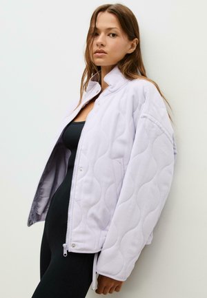Veste matelassée lavande clair avec col montant, fermeture éclair et poches latérales ; présente une texture lisse et une coupe surdimensionnée.