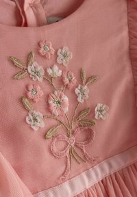 Rosa Kleid mit floraler Stickerei aus hellrosa und weißen Blumen, grünen Blättern und einer Schleifendetail, gefertigt aus strukturiertem Stoff.