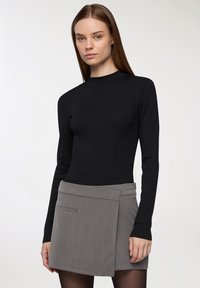 Czarna, długosleeve'owa bluzka wykonana z materiału prążkowanego, zestawiona z szaro A-liniową spódnicą z boczną kieszenią i usztywnioną konstrukcją.