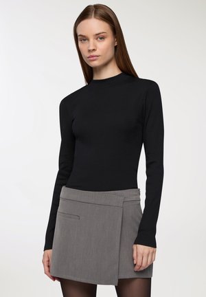 Top lungo nero a maniche lunghe realizzato in tessuto a coste, abbinato a una gonna grigia a trapezio con tasca laterale e un design strutturato.