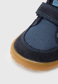 Tmavomodrá športová obuv s vrchným dielom z nylonovej sieťoviny a semišovými detailmi. Obsahuje suchý zips, svetlomodré prešívanie a podrážku z prírodnej gumy. Dizajn s okrúhlou špičkou.