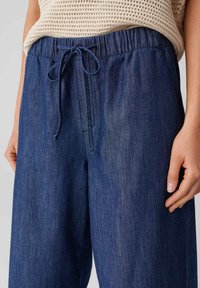 Dark blue denim jogger pants with an elastic waistband, drawstring front, and loose fit, featuring a subtle texture and no visible patterns.