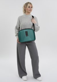 Teal hard-shell schoudertas met verticale ribbelstructuur, zwarte hardware accenten en een rechthoekig vak. Soepele, duurzame stof.