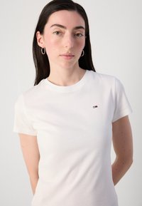 T-shirt bianco in cotone con collo tondo e maniche corte, caratterizzato da un piccolo logo multicolore sul petto sinistro. Tessuto liscio.