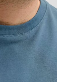 Blaues Baumwoll-T-Shirt mit Rundhalsausschnitt, glatter Textur und minimalen Nahtdetails am Kragen.