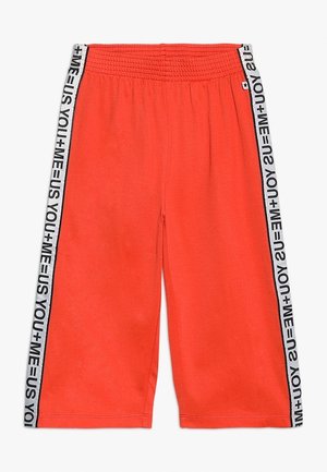 Lyseorange shorts med elastisk talje, med hvide sidelister med sort tekst, der gentagne gange lyder "YOU + ME = US".