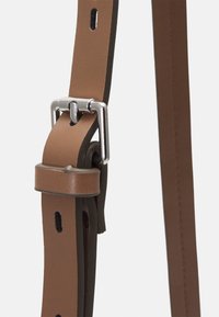 Gros plan d'une sangle en cuir marron avec une boucle rectangulaire argentée et des trous de réglage sur fond blanc.