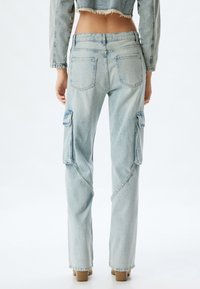 Pantalones cargo de mezclilla azul claro con bolsillos de parche, piernas rectas y dobladillo deshilachado en una chaqueta cortada. Textura suave, diseño casual.