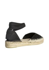 Espadrilles negras con suela de yute trenzado, diseño de punta abierta y tiras de tela que envuelven el tobillo. Presenta un tacón texturizado y acentos cosidos.