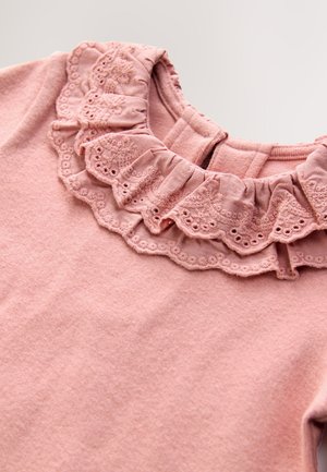 Lyserød tekstiltop med flæsekant og fin blonderdetalje samt en blød, struktureret finish. Lukning bagpå for nem påklædning.