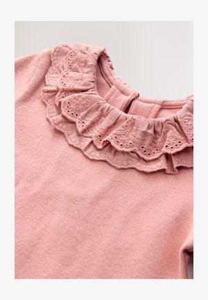 Top textil rosa con cuello fruncido que presenta detalles intrincados de encaje y un acabado suave y texturizado. Cierre en la parte trasera para facilitar su uso.