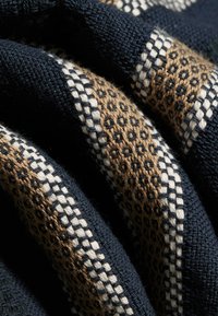 Gros plan sur un tissu bleu marine plié avec des motifs géométriques tissés beige et blancs et des détails tricotés texturés.