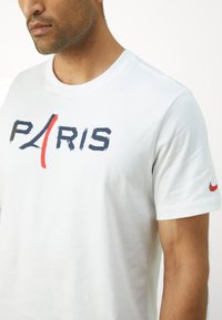 Hvid bomulds T-shirt med "PARIS" i marineblå og rød penselstrøgstekst på fronten og et lille rødt Nike-logo på ærmet.