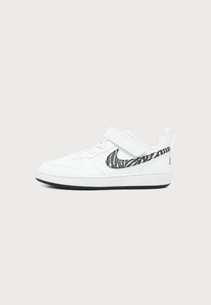 Λευκό sneaker χαμηλού τύπου με ασπρόμαυρο λογότυπο με ρίγες ζέβρας, λουράκι με βέλκρο και μαύρη σόλα σε ανοιχτό γκρι φόντο.