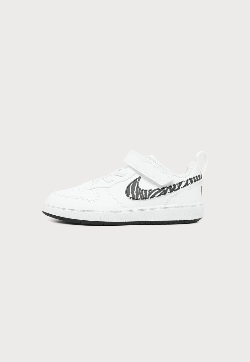 Λευκό sneaker χαμηλού τύπου με ασπρόμαυρο λογότυπο με ρίγες ζέβρας, λουράκι με βέλκρο και μαύρη σόλα σε ανοιχτό γκρι φόντο.