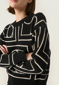 Czarny sweter dzianinowy z kremowymi geometrycznymi wzorami, ściągaczami na rękawach i okrągłym dekoltem. Teksturowany materiał z widocznymi detalami szycia.