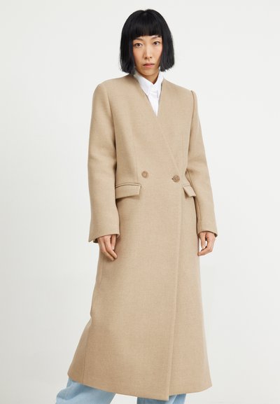 Beige wollen jas met een dubbelzijdig ontwerp, gesneden revers, zijzakken en lange mouwen. Gladde textuur, knielange snit, minimale details.
