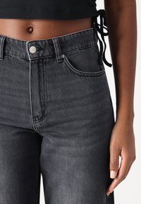 High-waisted black denim jeans with a smooth texture, five-pocket design, silver button closure, and contrast stitching details.