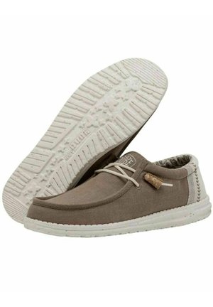 Zapatos de lienzo marrón con una suela de goma blanca, detalles de cordones, acentos texturizados y una etiqueta de corcho. Presentan un diseño cosido a lo largo de los lados.