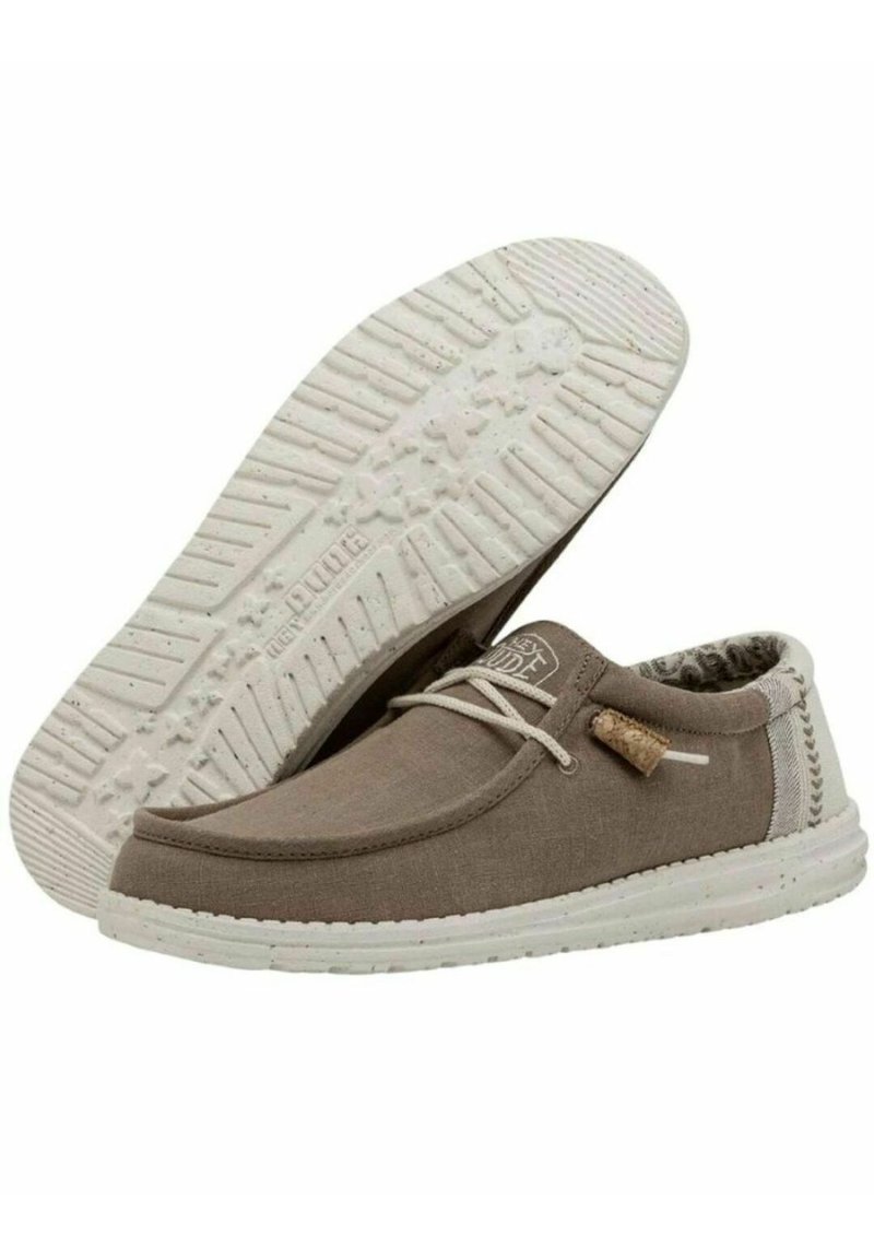 Scarpe in canvas marrone con suola in gomma bianca, dettagli in pizzo, accenti testurizzati e un'etichetta in sughero. Presentano un design cucito lungo i lati.