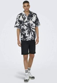 Short-sleeve, black and white palm print shirt paired with black shorts. The outfit features a casual fit and bold graphic design.