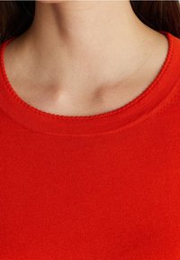 Red knit sweater featuring a smooth texture, wide round neckline, and ribbed trim. The fabric appears solid without patterns or accents.