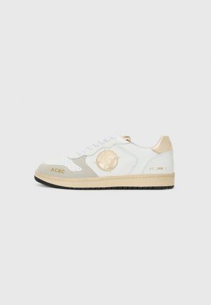 Fehér bőr sneaker bézs velúr díszítéssel, kerek logóval, arany betűzéssel és fekete gumi talppal. A futózsinórok fehérek.