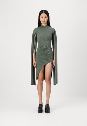 Robe vert olive avec un col haut, un design froncé, des manches longues, un ourlet asymétrique et une fente haute sur la cuisse, assortie à des chaussures noires.