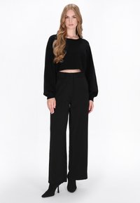 Zwarte cropped trui met lange mouwen, gecombineerd met hoge zwarte wijde broek en puntige zwarte hakken. Glad textuur.