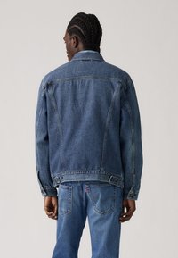 Chaqueta de denim de color azul desgastado, con bolsillos en el pecho, cierre de botones y un corte relajado. Presenta una tela texturizada y costuras en contraste.